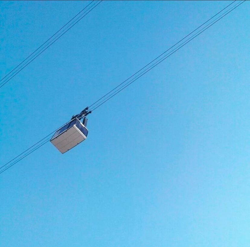 Imagen tomada desde abajo de una cabina del teleférico de Puebla, suspendida en el aire sobre cables gruesos, de fondo esta el cielo despejado y completamente azul.