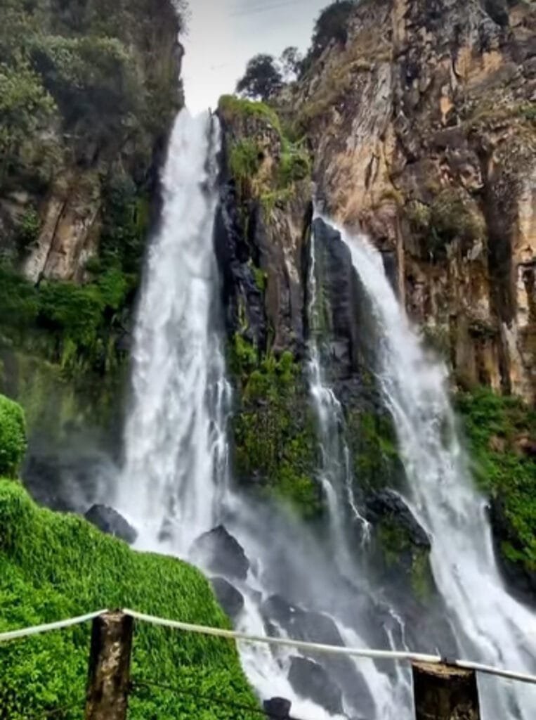 Rocas cafés con dos cascadas en donde de ellas cae una gran cantidad de agua. También se aprecia mucho el color verde.