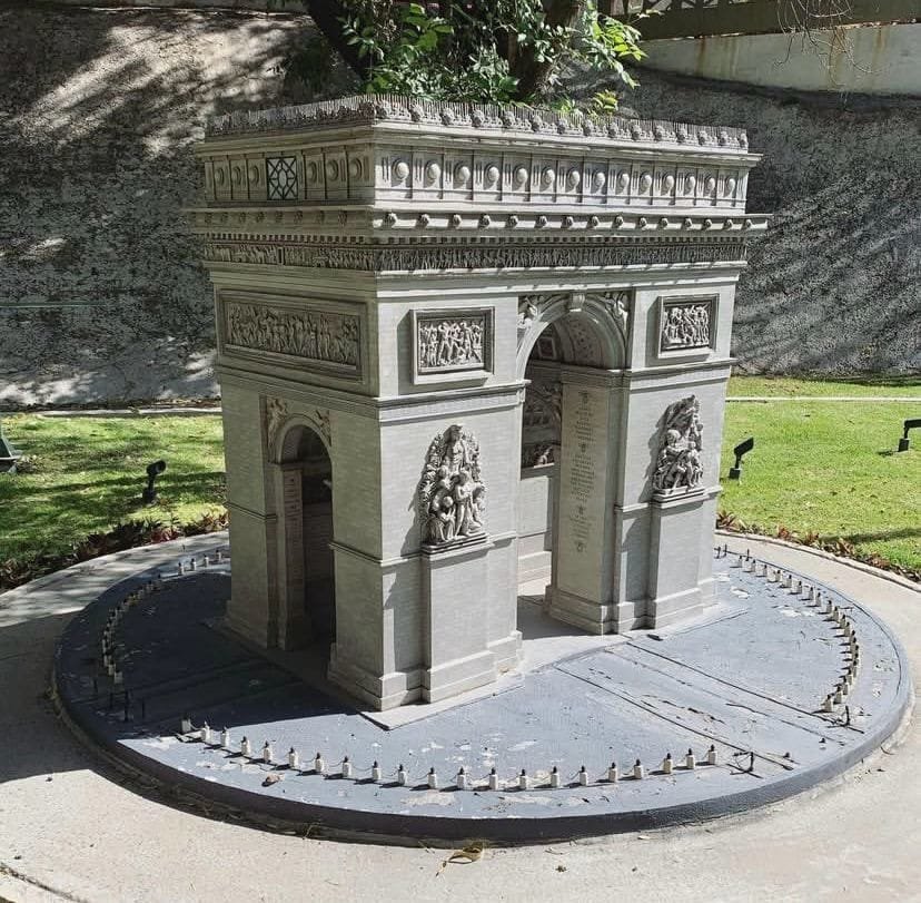 Maqueta a escala del Arco del Triunfo de París, Francia, ubicada en el Paseo de los Gigantes en Puebla. Al fondo se observa césped y un relieve rocoso.